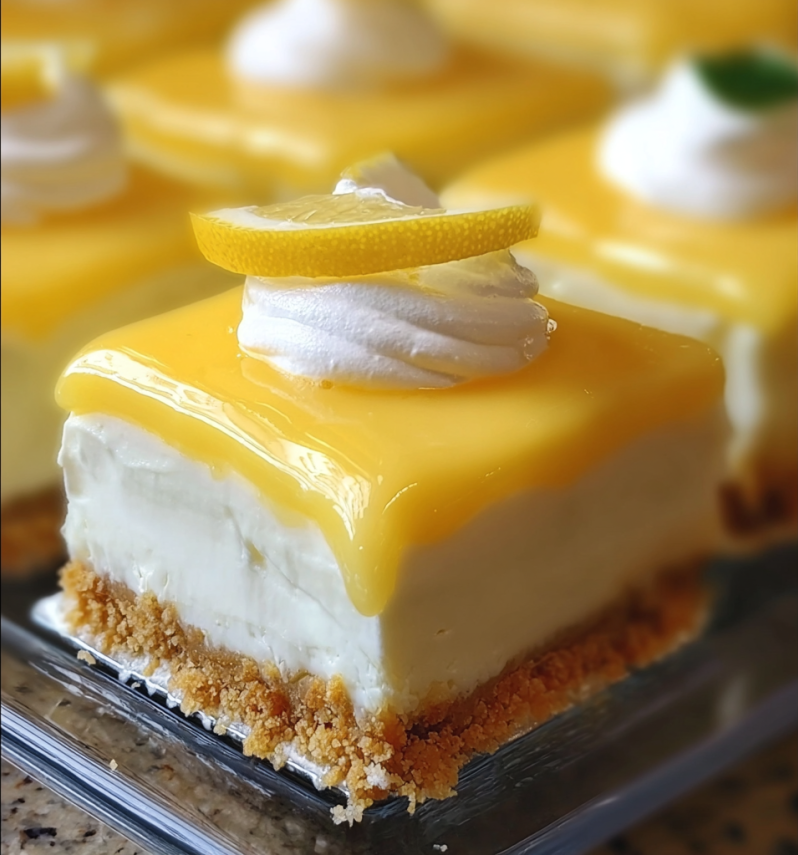 Three lemon cheesecake bars with powdered sugar, lemon wedges, and mint on a wooden board.
