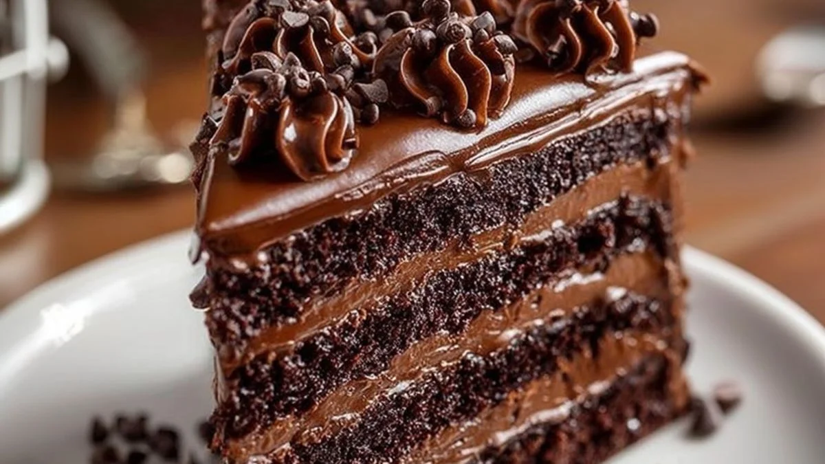 A slice of Midnight Chocolate Fudge Cake with glossy chocolate ganache and rich, moist layers