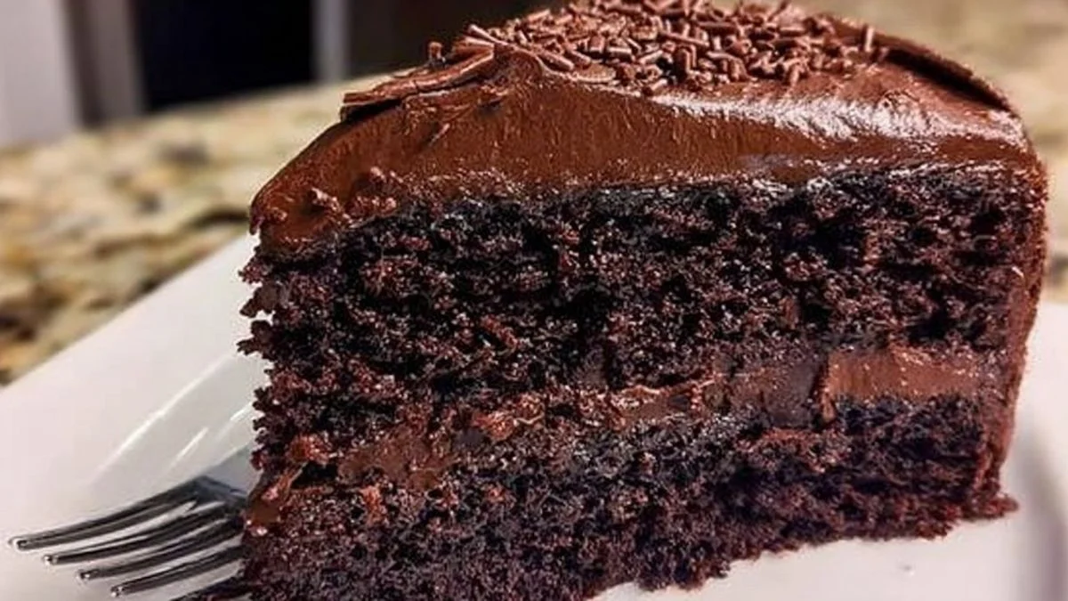 Slice of Midnight Fudge Cake with glossy chocolate ganache dripping in a moody, candlelit setting