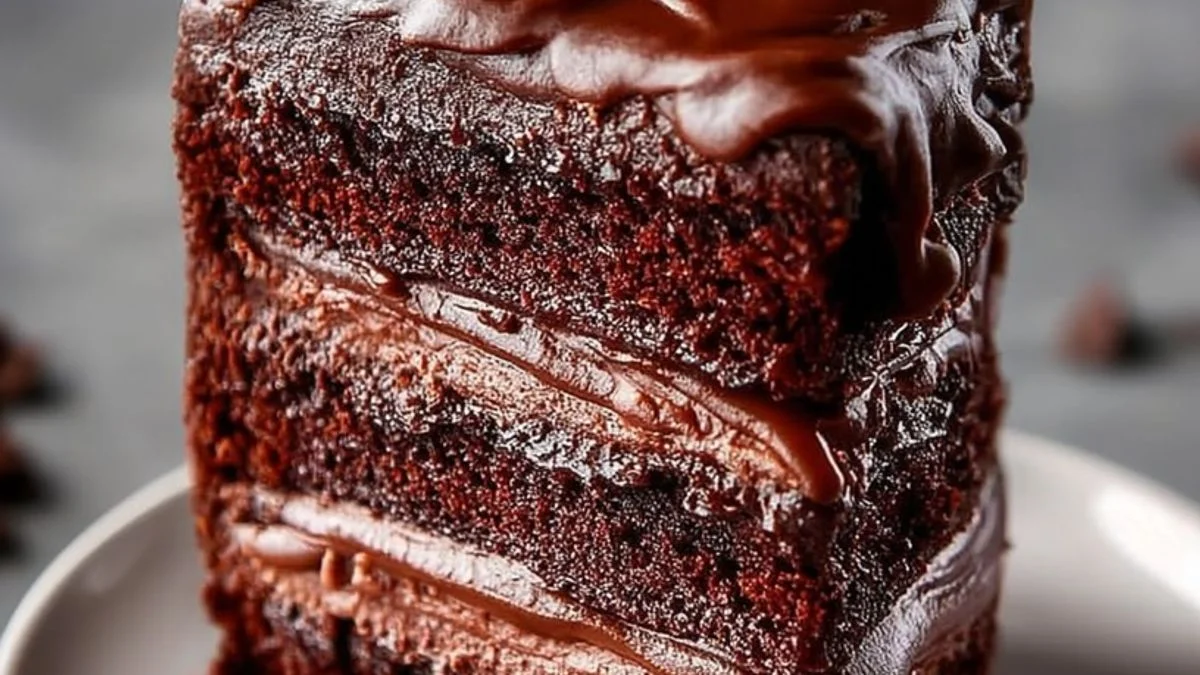 A slice of the Ultimate Fudge Chocolate Cake with glossy ganache and chocolate shavings on a white plate.