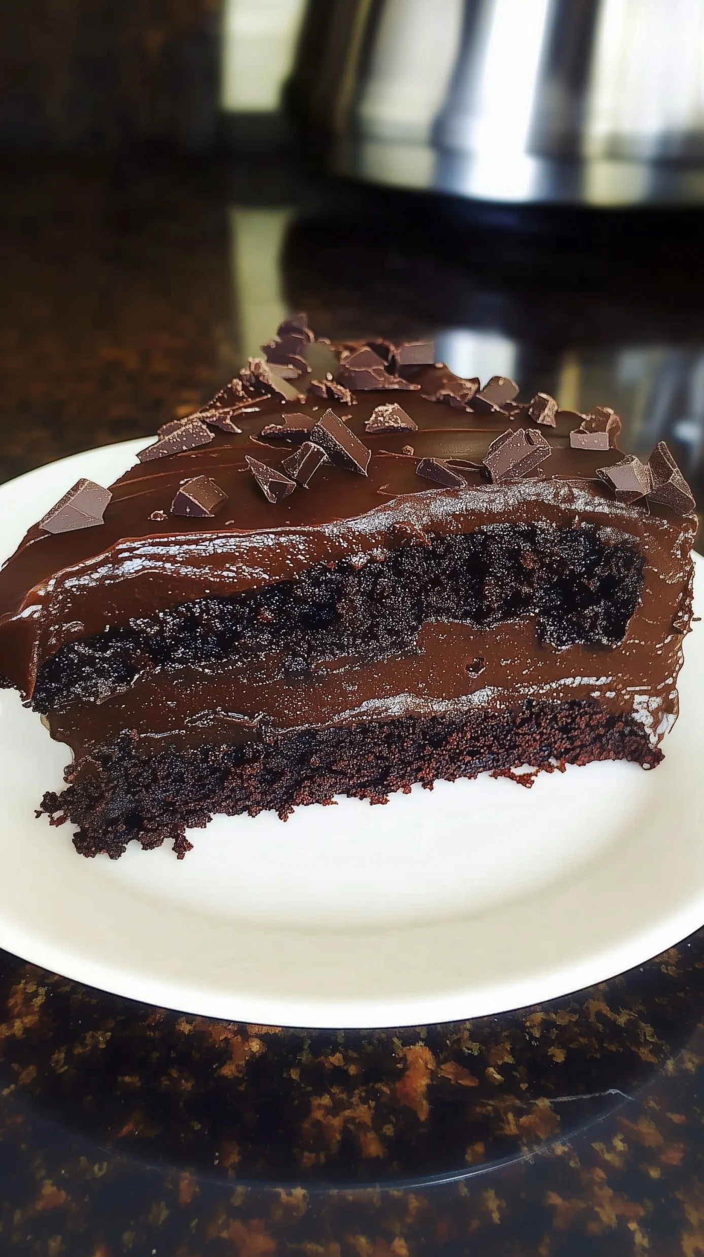 Slice of ultimate fudge cake with glossy chocolate ganache on a wooden board