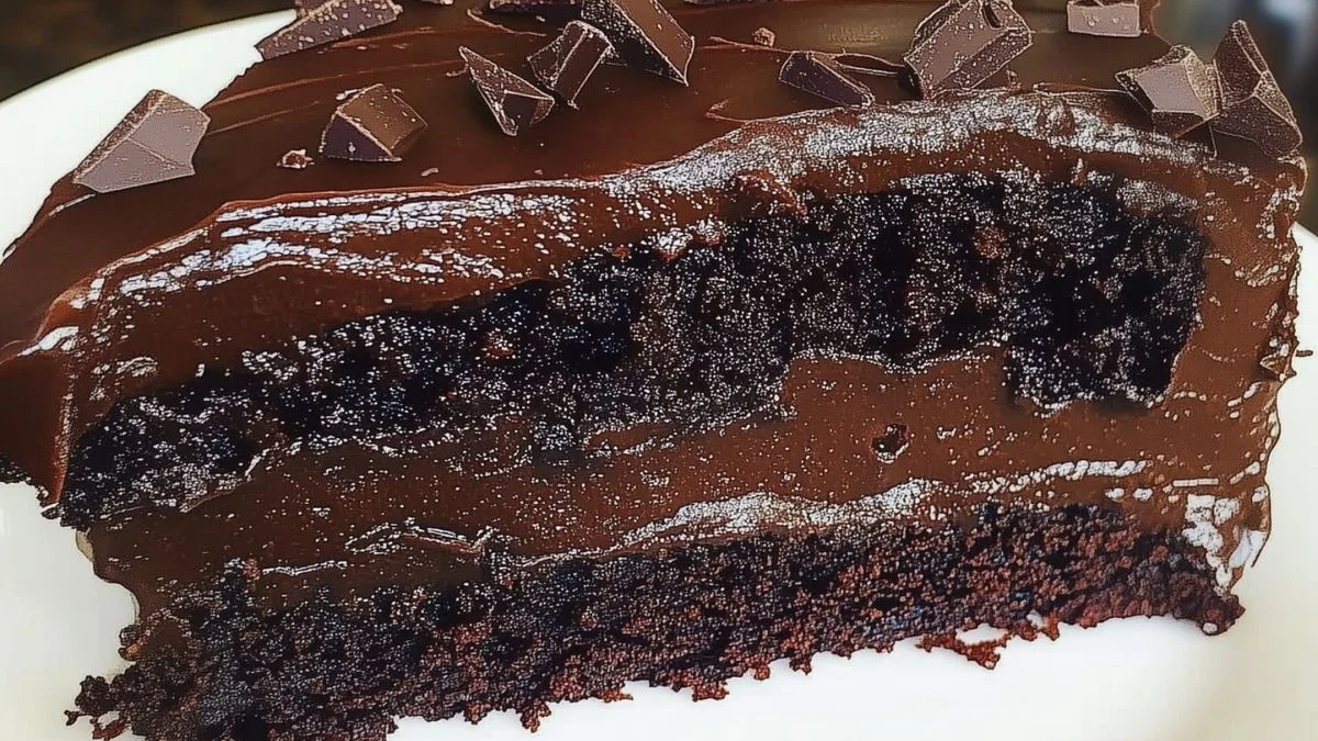 A slice of Ultimate Fudge Cake with glossy chocolate ganache and fresh raspberries